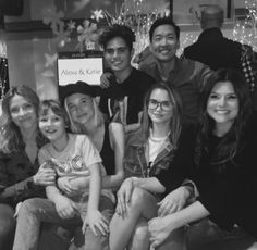 a group of people sitting next to each other in front of a christmas tree with lights