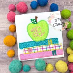 an apple on top of a pile of books surrounded by pom poms