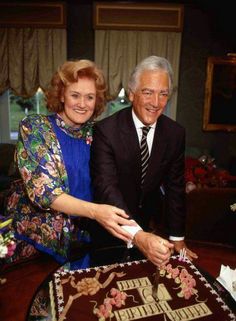 an older man and woman cutting into a chocolate cake with the word happy birthday written on it