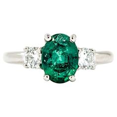 an emerald and diamond ring with three diamonds on the side, set in white gold