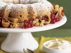 a bundt cake with berries and powdered sugar sits on a plate next to a bowl of whipped cream