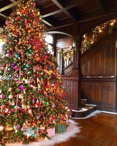 a decorated christmas tree in the middle of a room with wood paneling and stairs