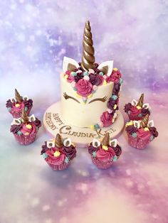 there is a white cake with pink frosting and an unicorn horn on top, surrounded by cupcakes