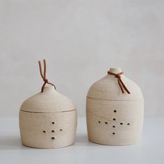 two white ceramic containers with brown string tied around the top one has holes in it