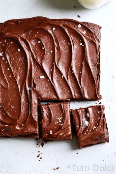 chocolate frosted brownies cut into squares and placed on a white surface next to a glass of milk