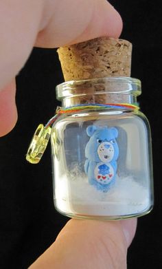 a hand holding a tiny glass jar with a bear in it