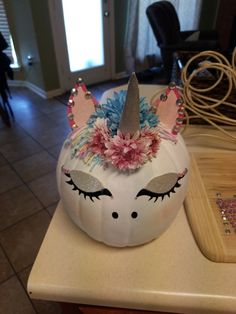 a white pumpkin decorated with an unicorn's face and flowers on it sitting on a counter