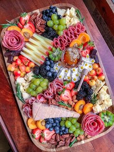 a wooden platter filled with different types of cheeses and fruit on top of a table