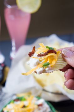 a person holding a cracker with cheese and bacon on it next to other snacks