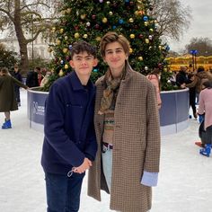 two people standing next to each other in front of a christmas tree and ice rink