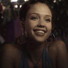 a woman smiling and wearing large hoop earrings in front of a christmas tree with lights on it