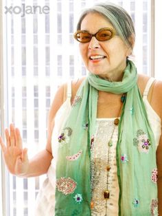 an older woman wearing sunglasses and a green scarf is standing in front of a window