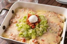 a casserole dish with cheese and lettuce in it on a wooden table