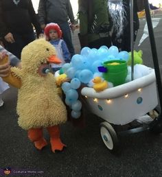 a child in a duck costume pushing a wagon with balloons on it and people standing around