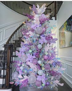 a purple and silver christmas tree in the middle of a spiral stair case with ornaments on it