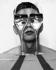 a man with three wine glasses in front of his face and the reflection of two people's faces