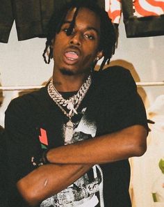 a young man with dreadlocks standing in front of clothes hanging on a rack