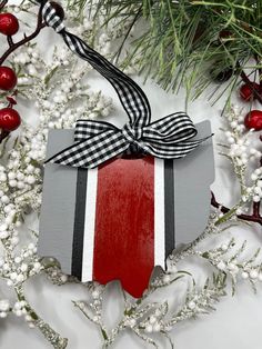 a christmas ornament with a ribbon and bow on it, surrounded by holly branches