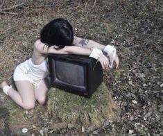 a woman sitting on the ground in front of a small tv that is turned upside down