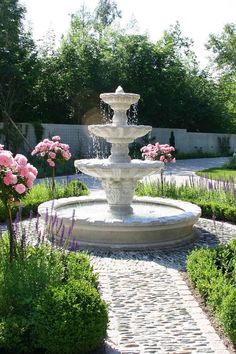 a white fountain surrounded by pink flowers and greenery in the middle of a garden