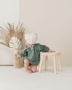 a small child sitting on a stool in front of a vase with dried grass and a plant