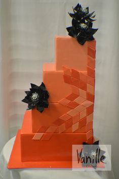 a three tiered cake with black flowers on the top and an orange block design