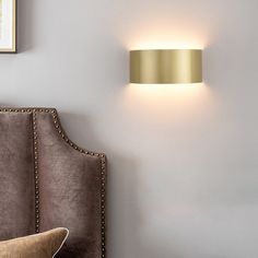 a wall light mounted on the side of a white wall next to a brown headboard