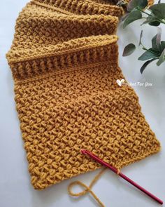 a crocheted yellow scarf next to a knitting needle