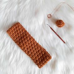 an orange crochet headband next to a knitting needle and ball of yarn