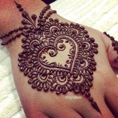 a henna tattoo on someone's hand that is decorated with beads and a heart