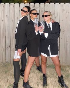 three women dressed in black and white posing for the camera with one holding a silver object