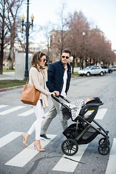 a man and woman walking across the street with a baby in a stroller next to them