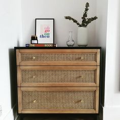 a wooden dresser sitting next to a wall with a vase on top of it and a plant in the corner