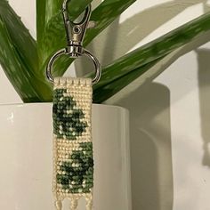 a green and white beaded keychain hanging from a metal hook next to a potted plant