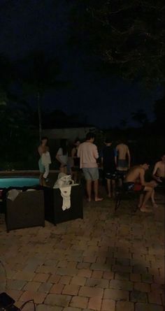 a group of people standing around a pool at night