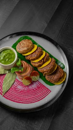 a white plate topped with meat patties and veggies next to a bowl of green sauce