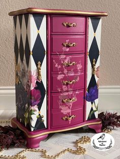 a pink and black dresser sitting on top of a white table next to a gold chain