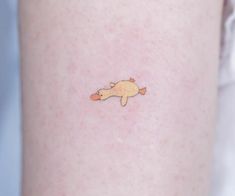 a small fish tattoo on the back of a woman's leg, it is yellow and orange