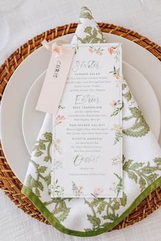 a table setting with place cards and napkins on top of the plate, next to a wicker basket