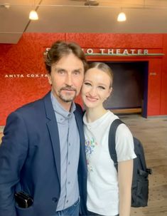 a man and woman standing next to each other in front of a red theater sign