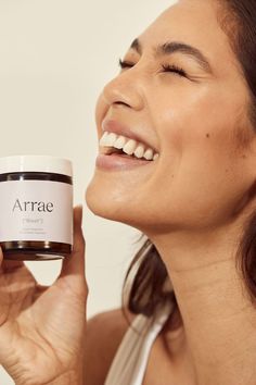 a woman holding up a jar of arraie cream to her face and smiling