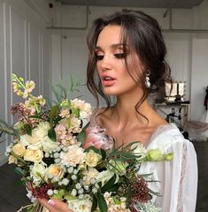 a woman holding a bouquet of flowers in her hands and looking at the camera while wearing a white dress