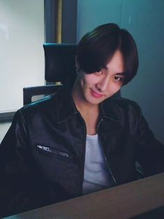 a person sitting at a desk in front of a laptop computer and wearing a black leather jacket