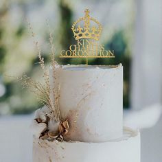 a white cake with gold decorations and a crown topper on it's side