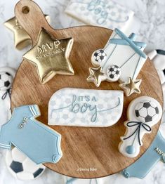 some cookies are on a wooden plate with soccer balls and stars in the shape of baby's clothes