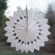 a white paper snowflake hanging from a string in front of a window with trees behind it