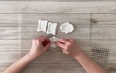 two hands are decorating small pieces of paper on a table with wood planks