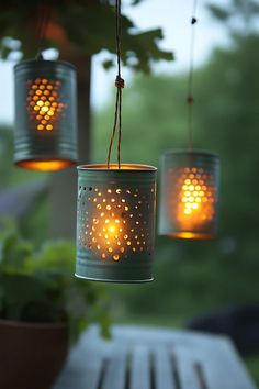 three mason jars with lights hanging from them on a patio table in front of trees