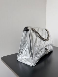 a silver handbag sitting on top of a black table next to a white wall