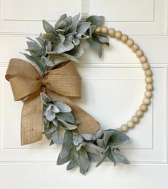 a wreath made out of wood beads and greenery hangs on a door with a burlap bow